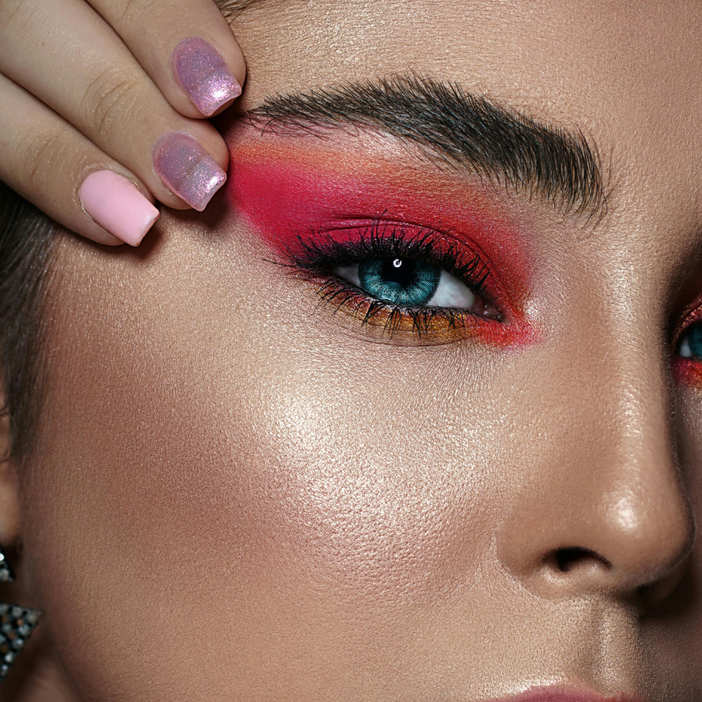 Close-up of a person's eye with vibrant makeup and a hand adjusting the hair.