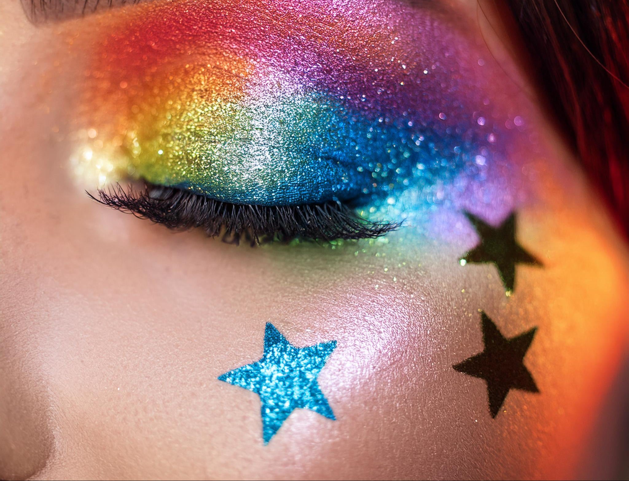 Close-up of a person's eye with colorful glitter makeup and star-shaped stickers.
