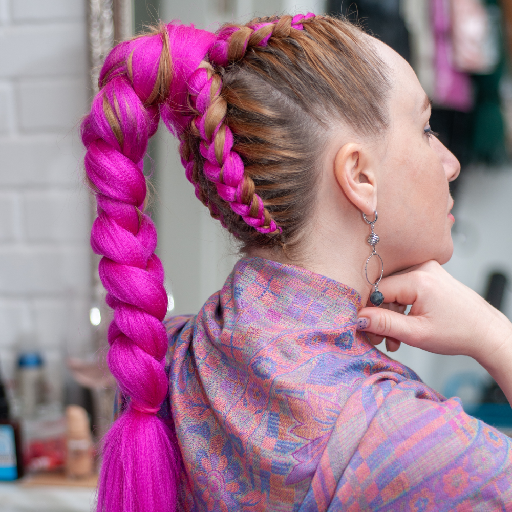 Woman with pink braided hair wearing a colorful scarf, indoors.
