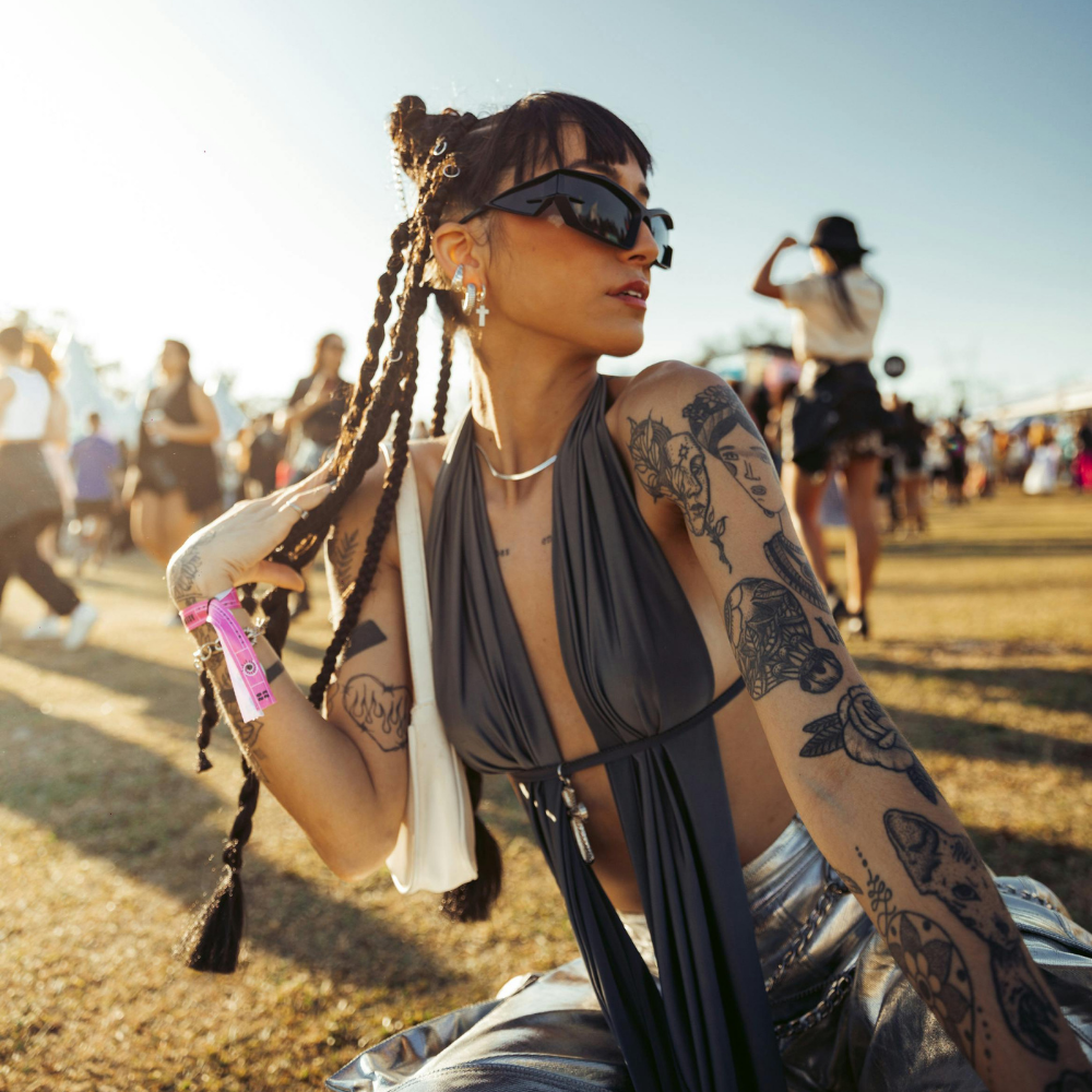 Woman with tattoos at a music festival, wearing sunglasses and a gray top.