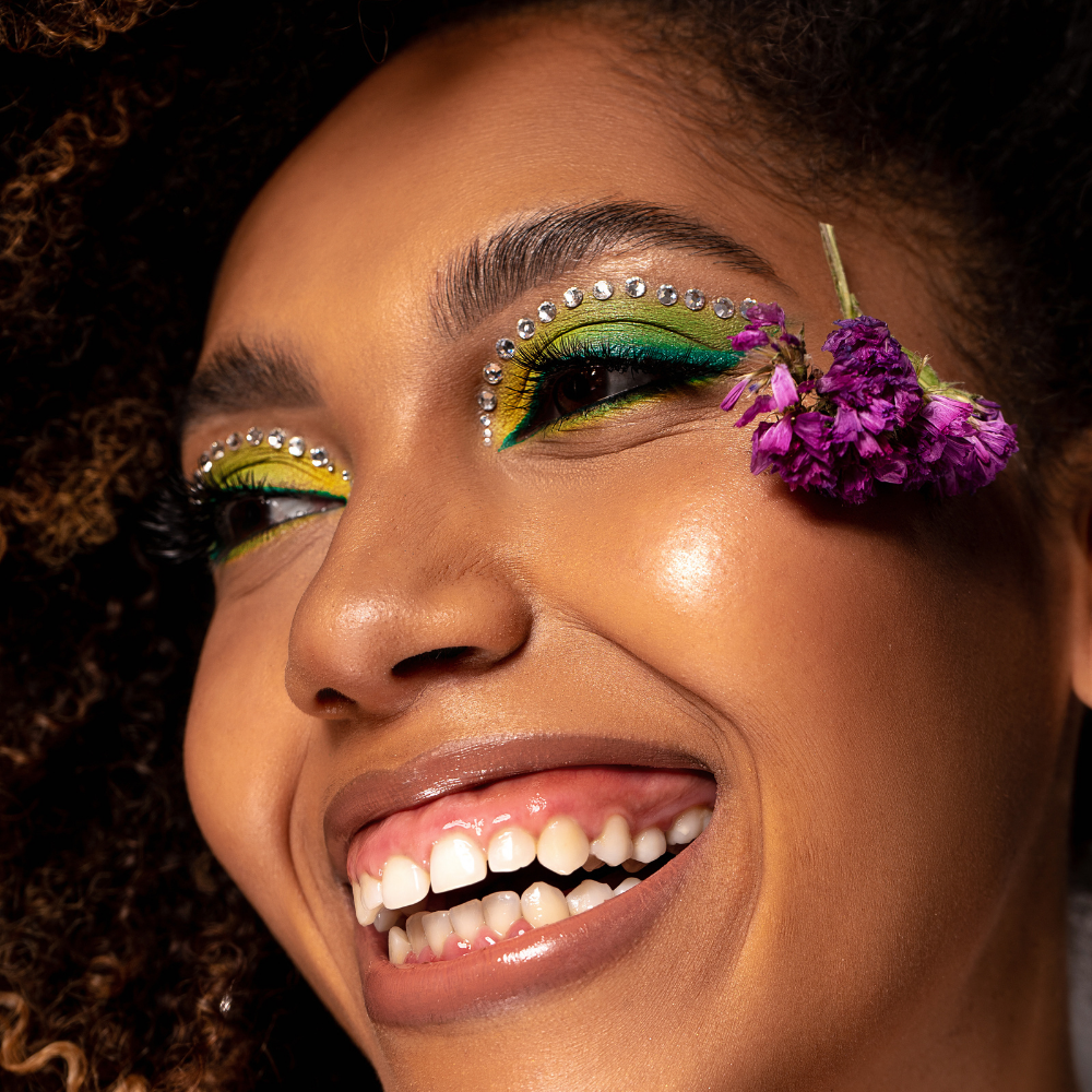 Close-up of a person with colorful eye makeup and a purple flower in their hair.